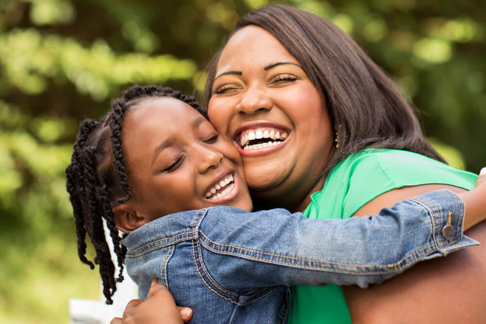 Black mother hugging her daughter, both smiling and happy.