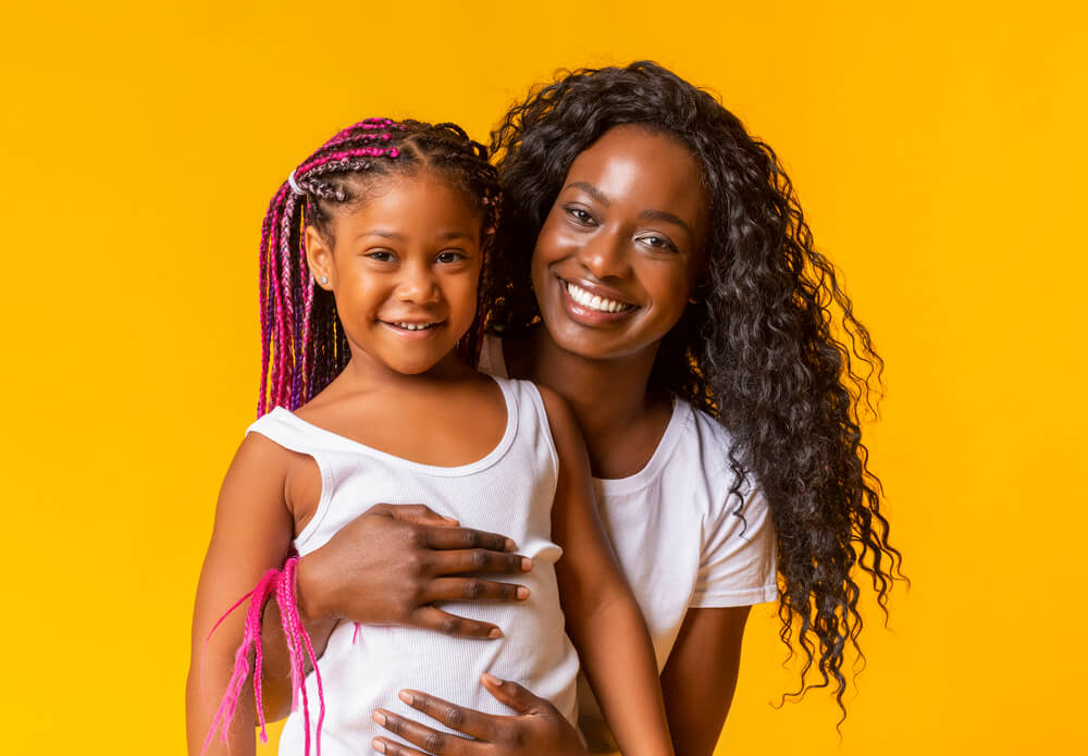 Black mother hugging daughter against a yellow background.
